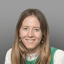 Smiling woman with long blonde hair, wearing a white collared shirt and a green knitted sweater vest.