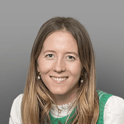 Smiling woman with long blonde hair, wearing a white collared shirt and a green knitted sweater vest.