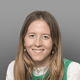 Smiling woman with long blonde hair, wearing a white collared shirt and a green knitted sweater vest.